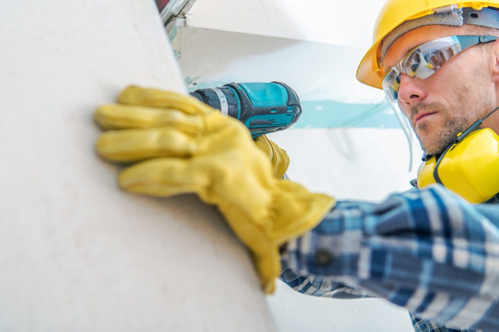 Contractor Remodeling Job. Caucasian Worker with Cordless Driller Installing Drywall Elements. Hard Hat Construction Zone